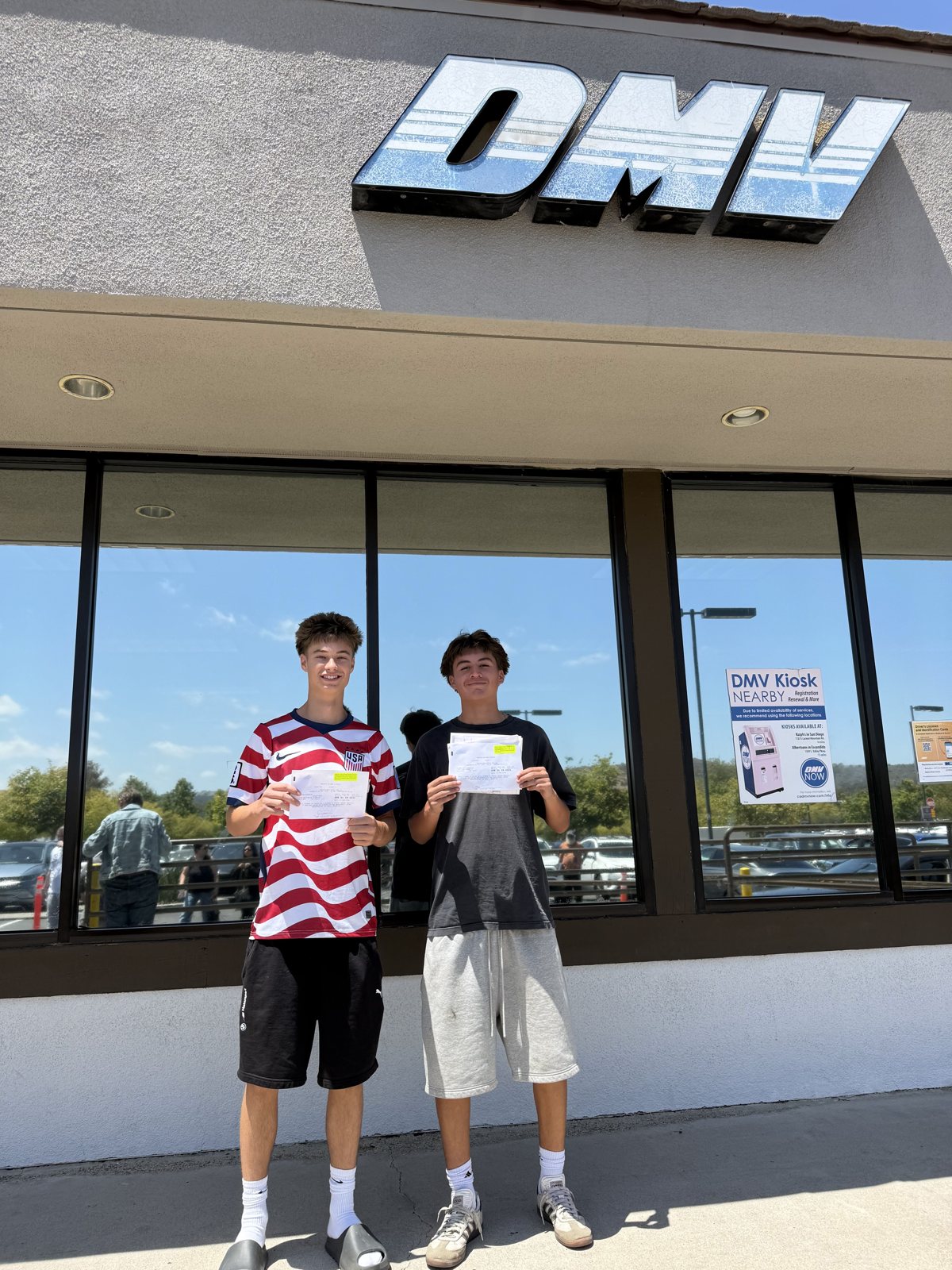 Two Pioneer Driving School students holding license paperwork outside the DMV after passing their driving tests